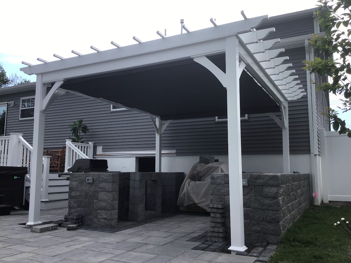 White vinyl pergola over a paver patio with a retractable fabric canopy drawn beneath the rafters