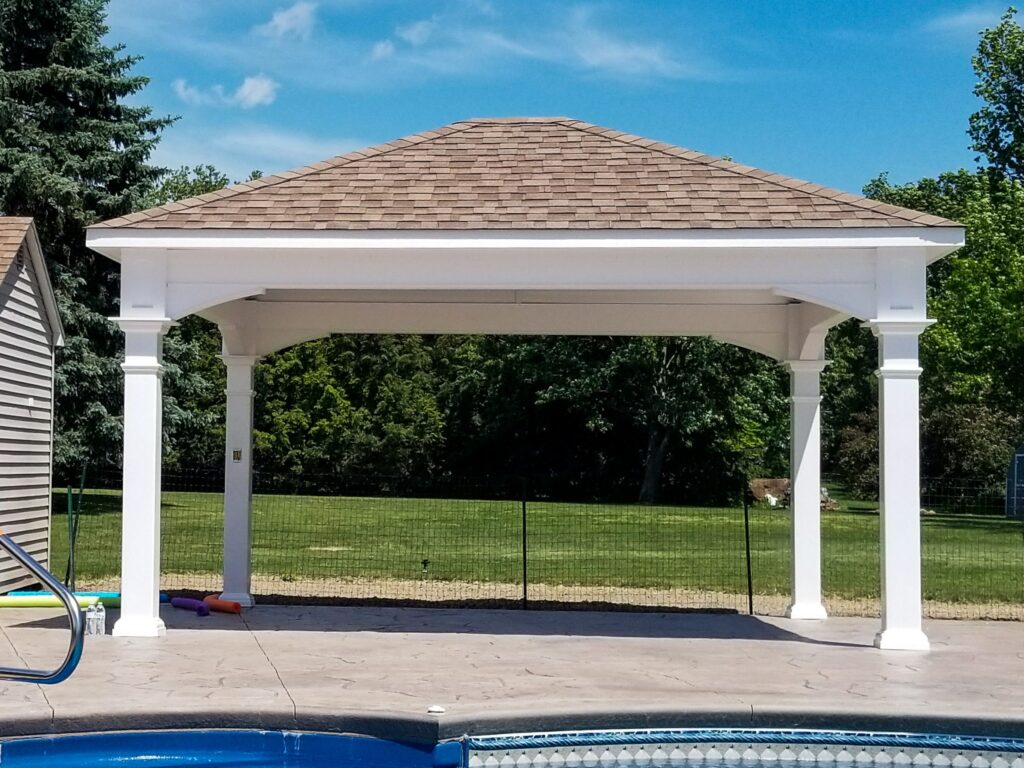 White vinyl pavilion with a shingled hip roof and open sides on a stamped concrete pool deck