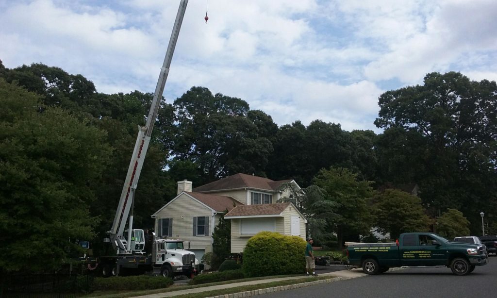 Crane truck and company pickup on a residential street preparing to lift a shed into a backyard